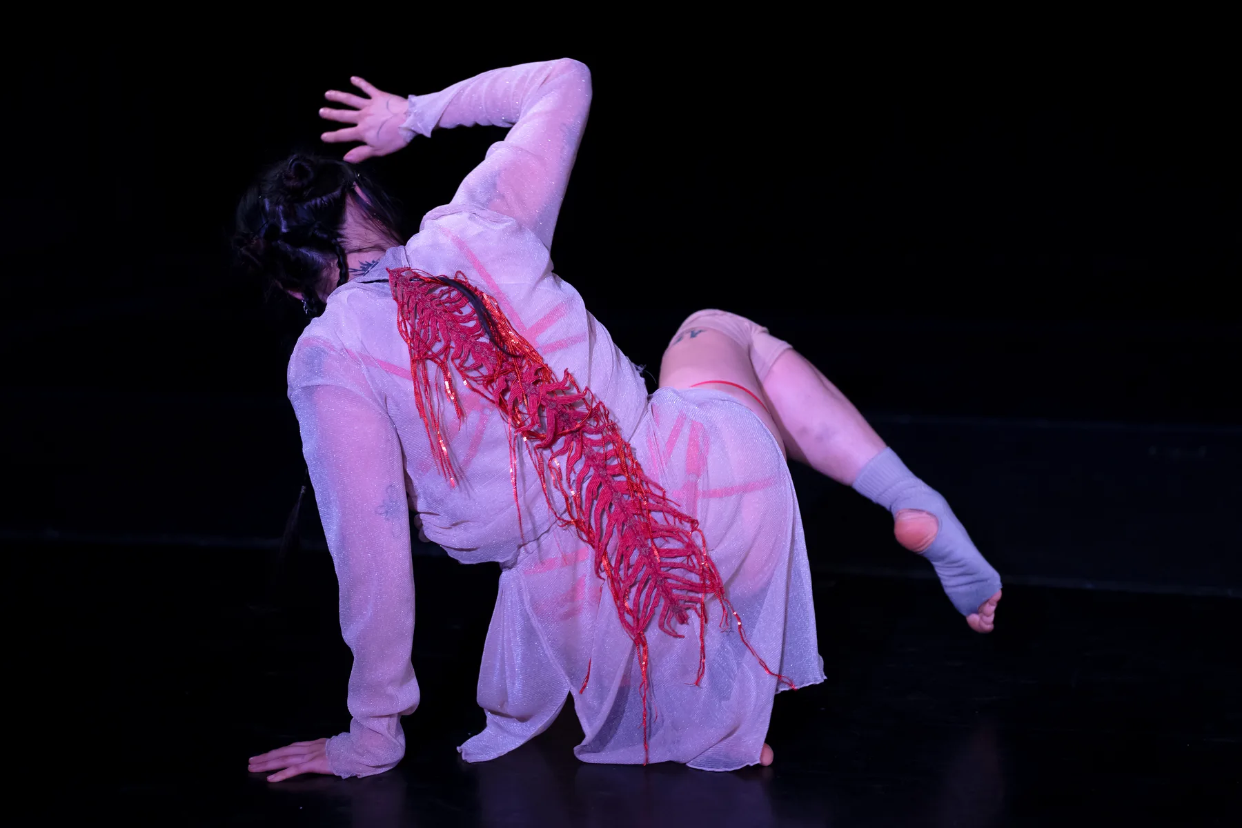 Lux Gow-Habrich performing Blood Song on the floor in a white costume with red beaded work.