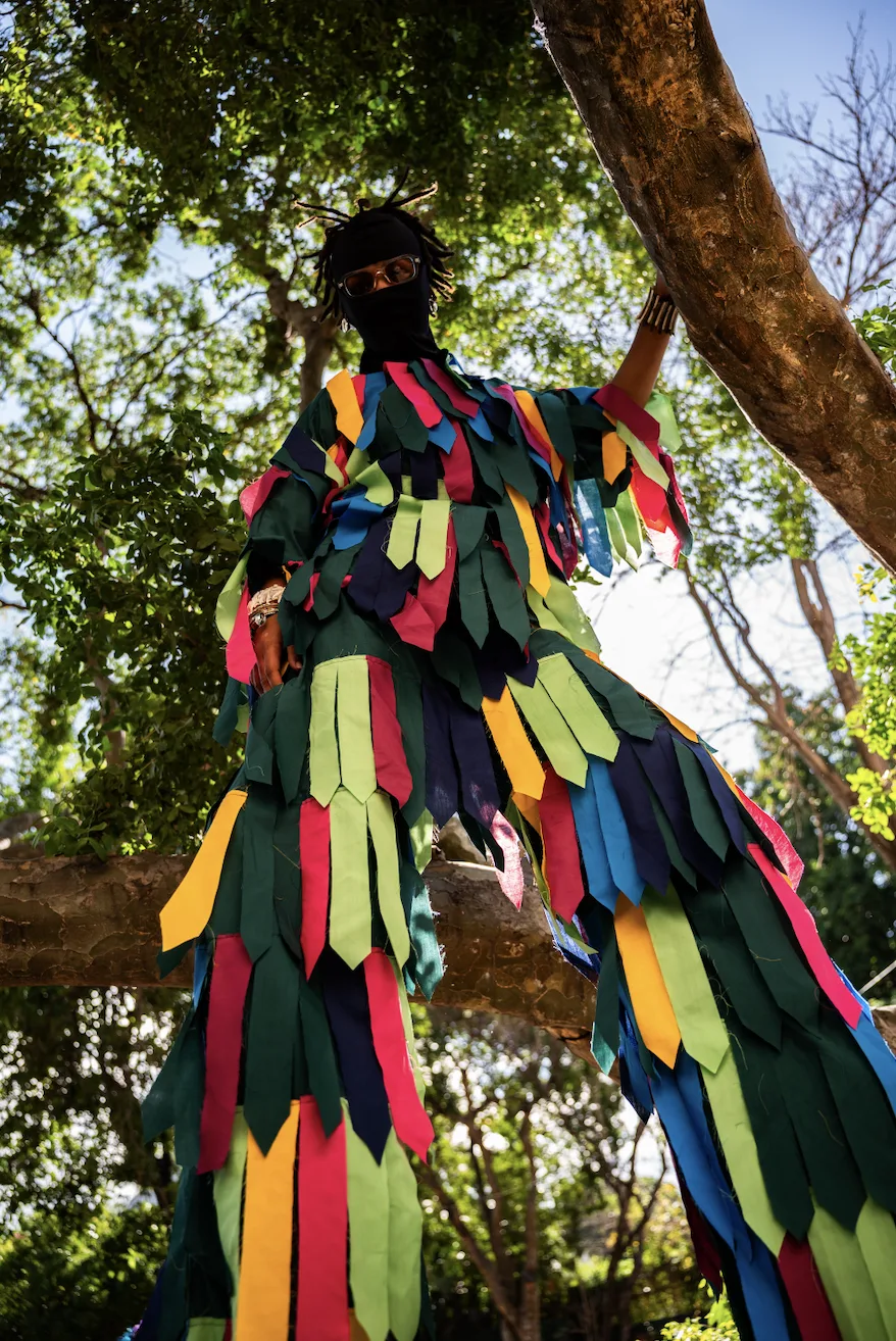 Pixel Heller in a colorful Moko Jumbie costume standing outdoors at height.